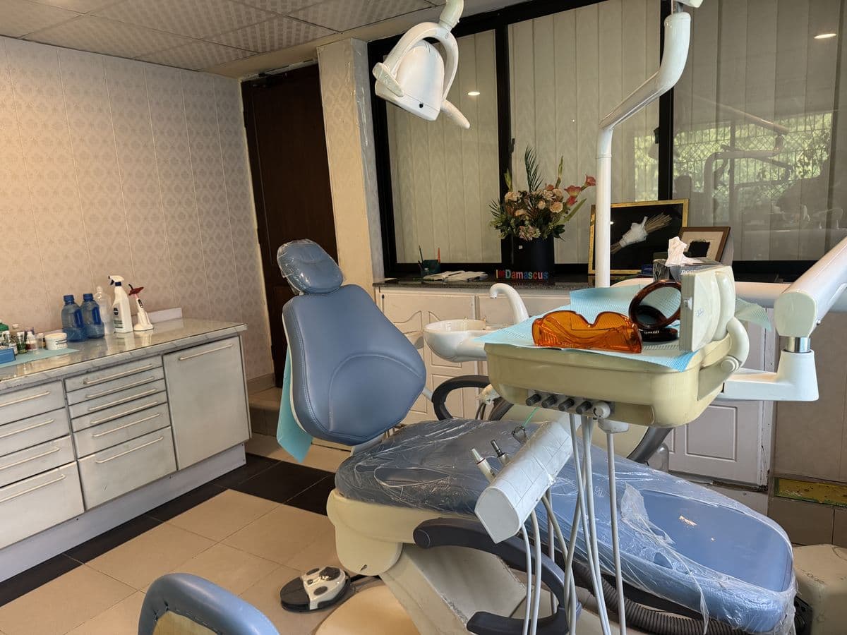 A treatment room with a dental chair, instrument cabinets and fresh flowers.